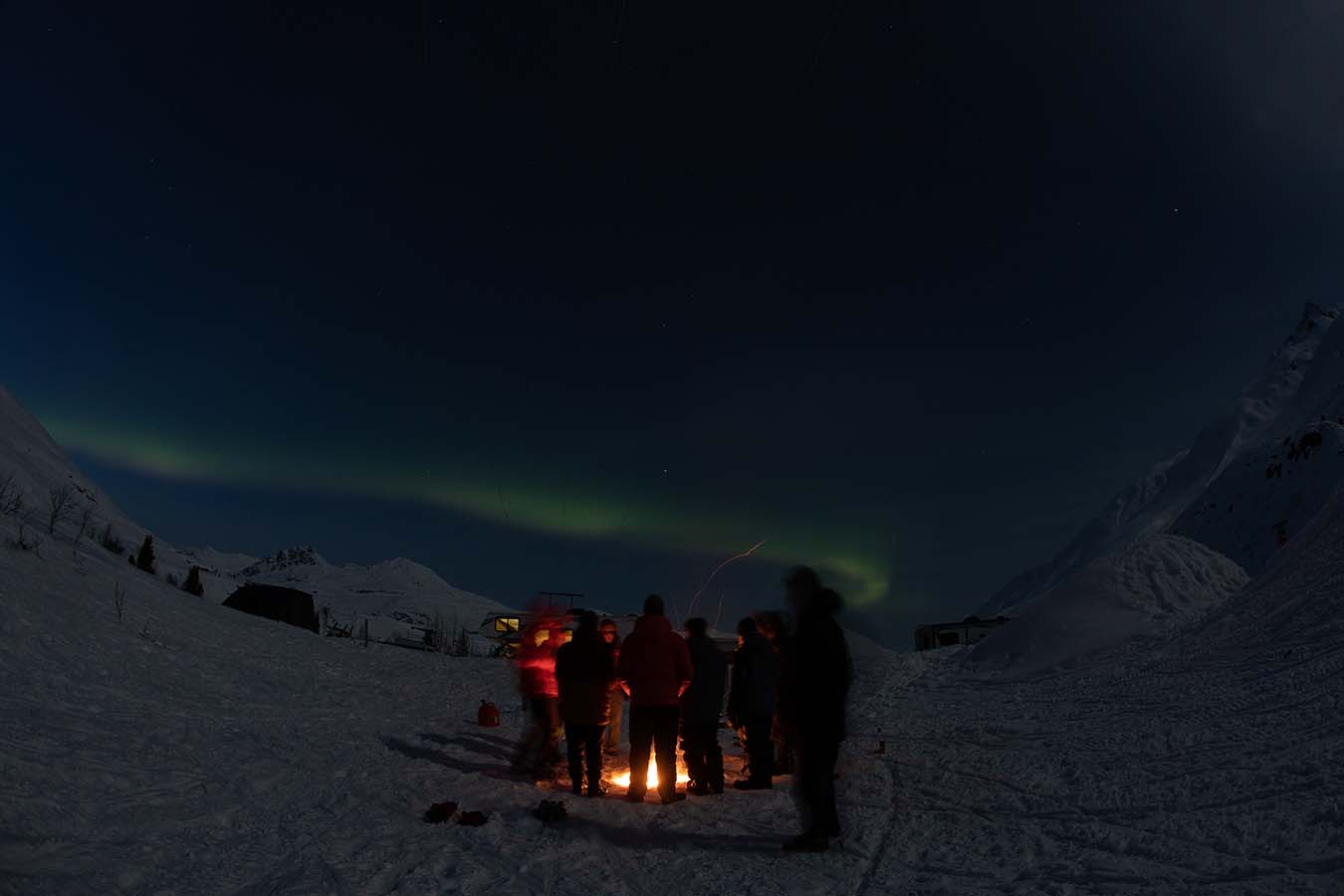 The group gathered around a camp fire, aurora borealis visible in the night sky