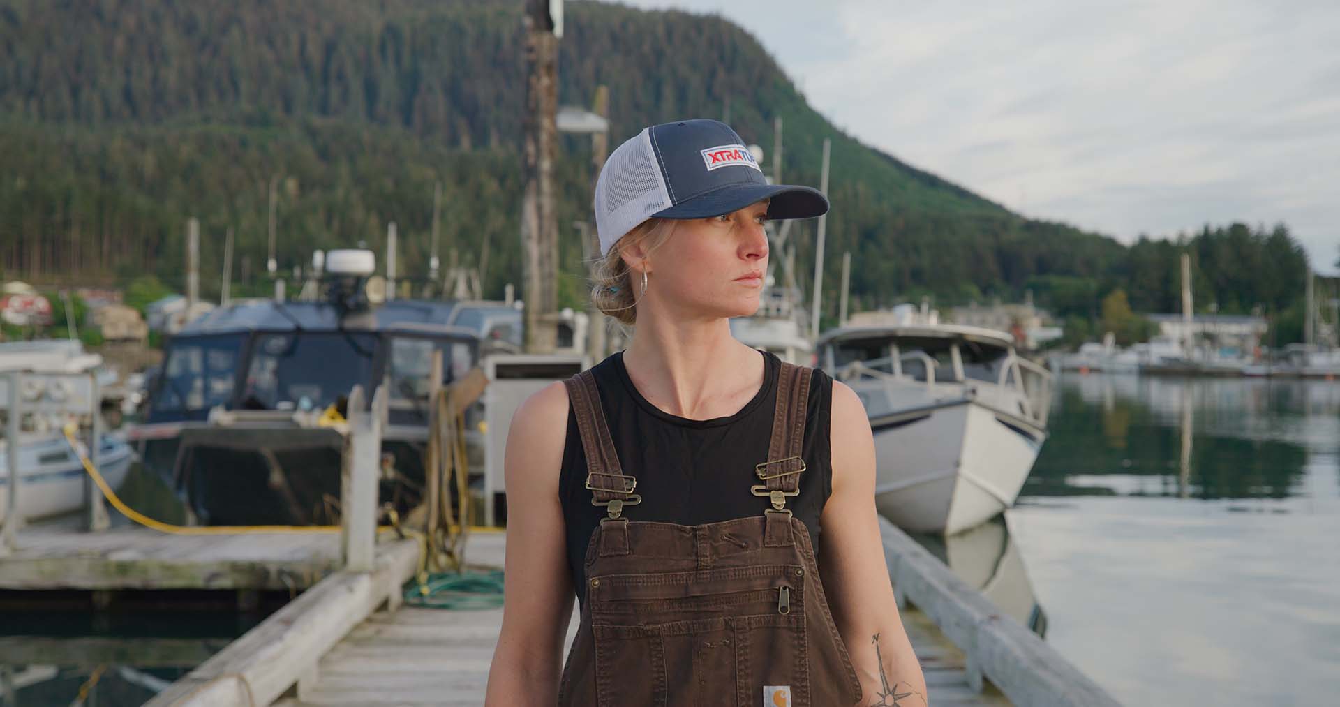Mckenna Peterson, wearing a cap and brown overalls, gazing on a water body.