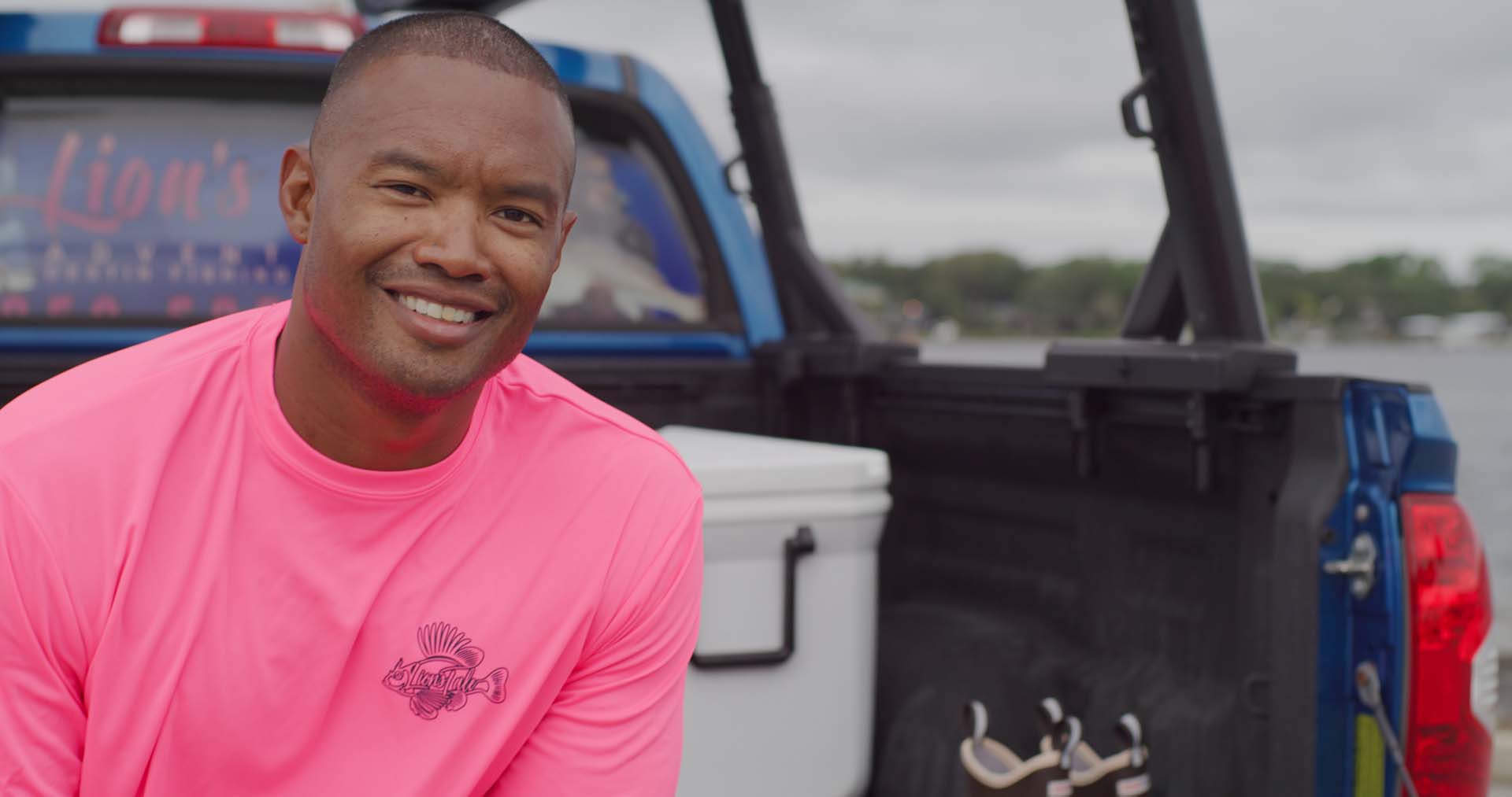 Lionel, in a bright pink shirt sitting on the bed of a pickup truck
