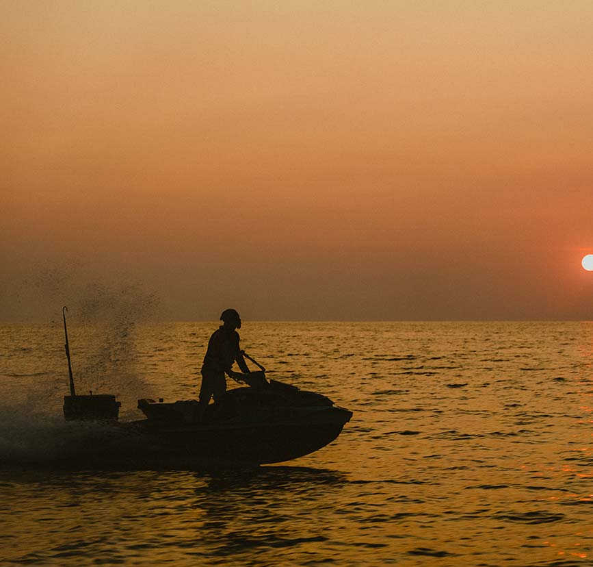The siloutte of a person riding a jet ski in the ocean in the orange ambiance of a sunset.