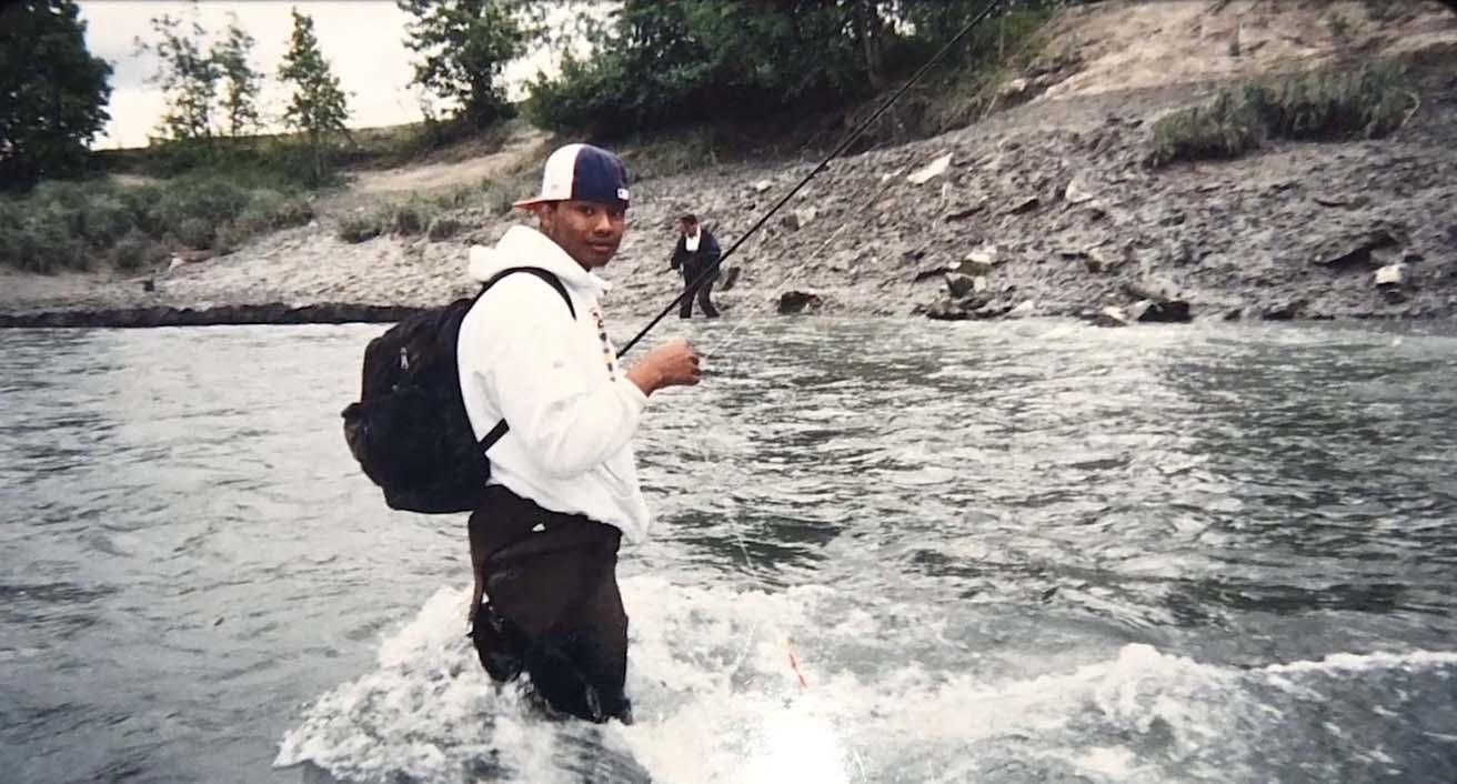 Lionel knee deep in water, casting a fishing line