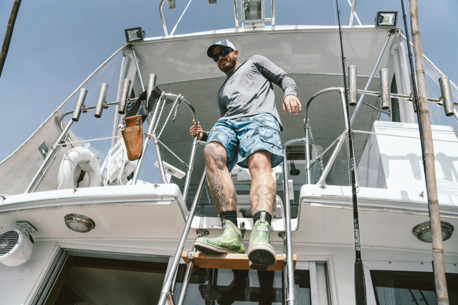 Man descending ladder on a fishing boat in Xtratuf boots. 