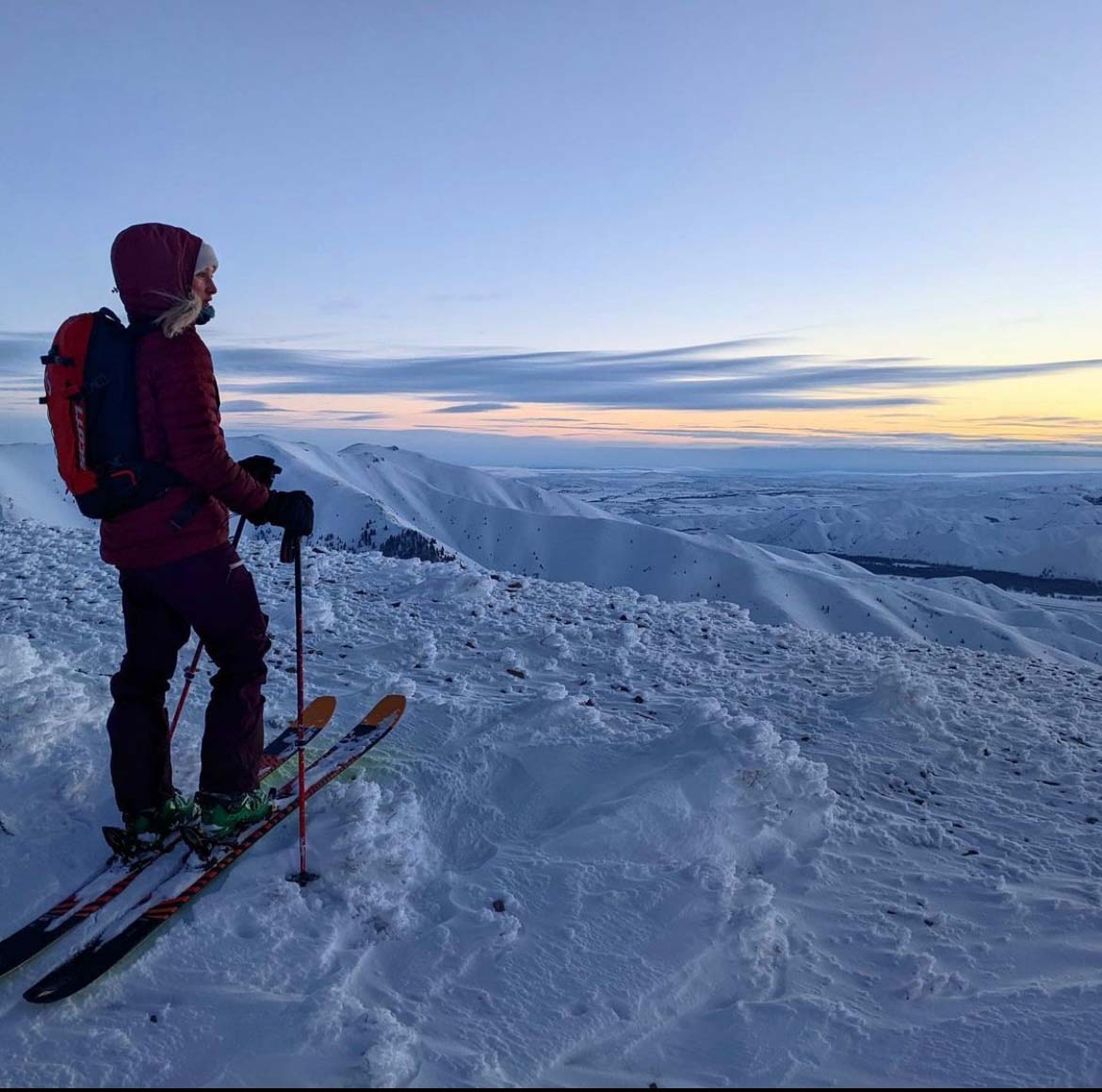 McKenna, standing on skis, gazing from a snowy mountain towards the horizon.