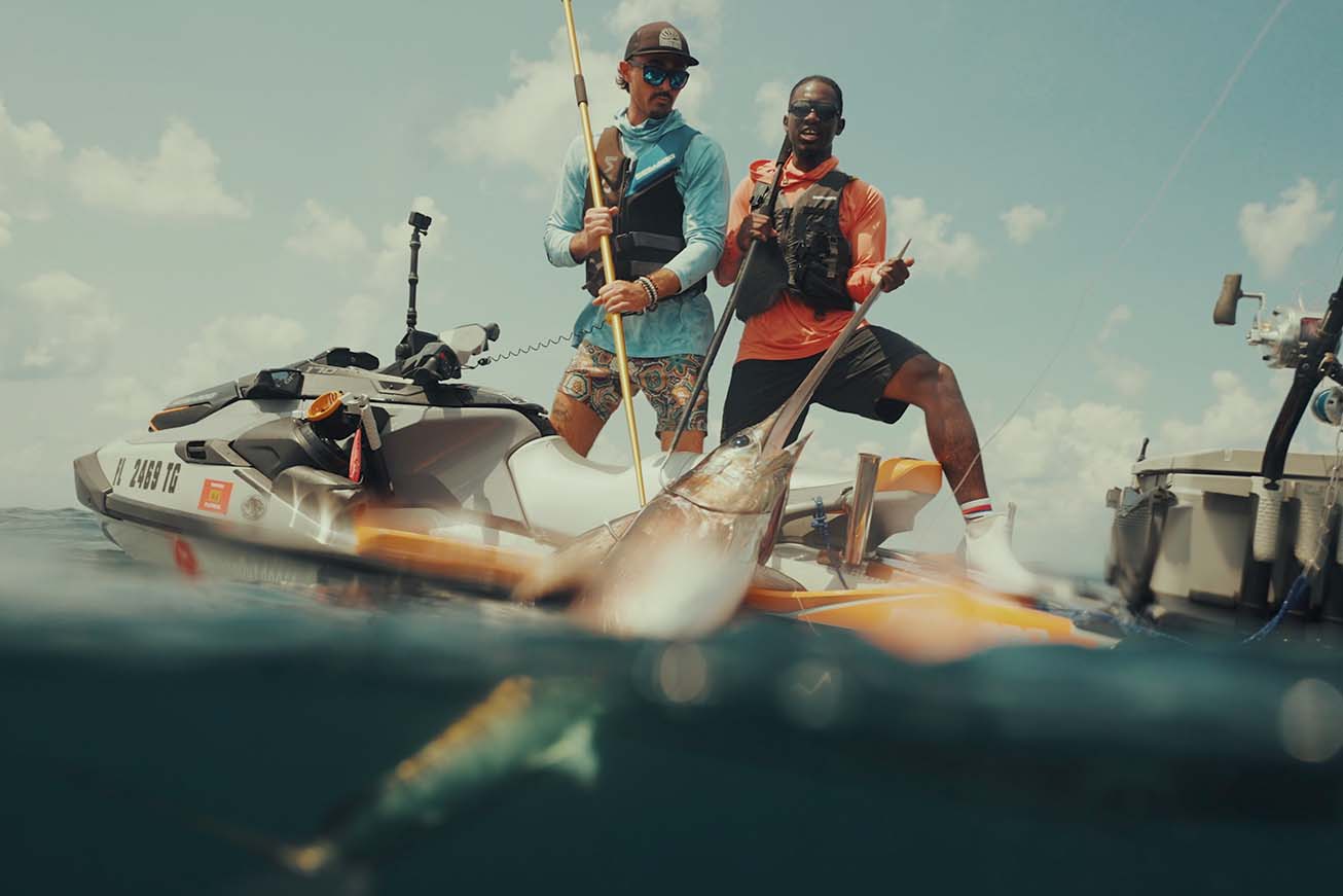 Emmanuel and another man initially pulling the swordfish from the water, and onto the jet ski.