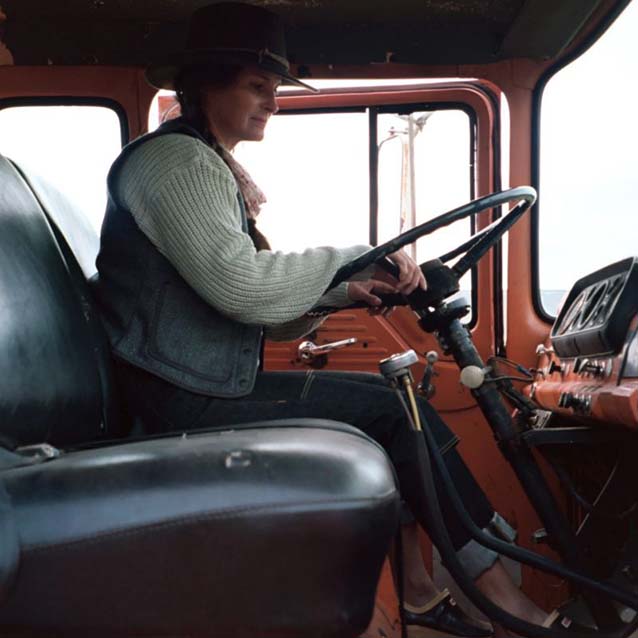 Corey sitting in a large old school truck, with her hands on both sides of the steering wheel.