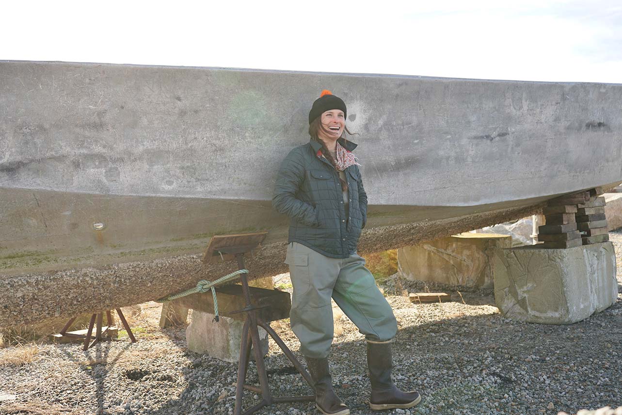 Corey leaning against a boat that is propped on concrete blocks on land.