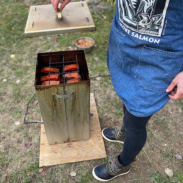 McKenna placing the lid on the smoker with the salmon tightly tucked on the wire rack inside.