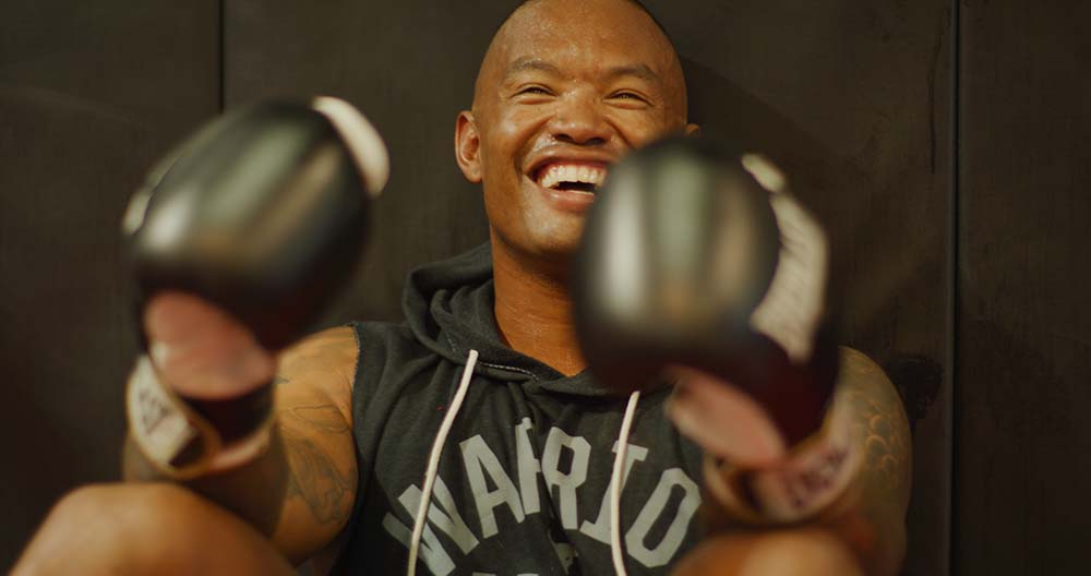 Lionel wearing a set of black boxing gloves and smiling widely.