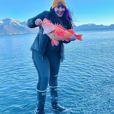 A woman wearing XTRATUFs holding up a large fish