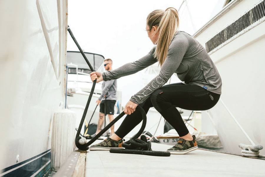 Lady wearing Xtratuf shoes tying up a boat. 