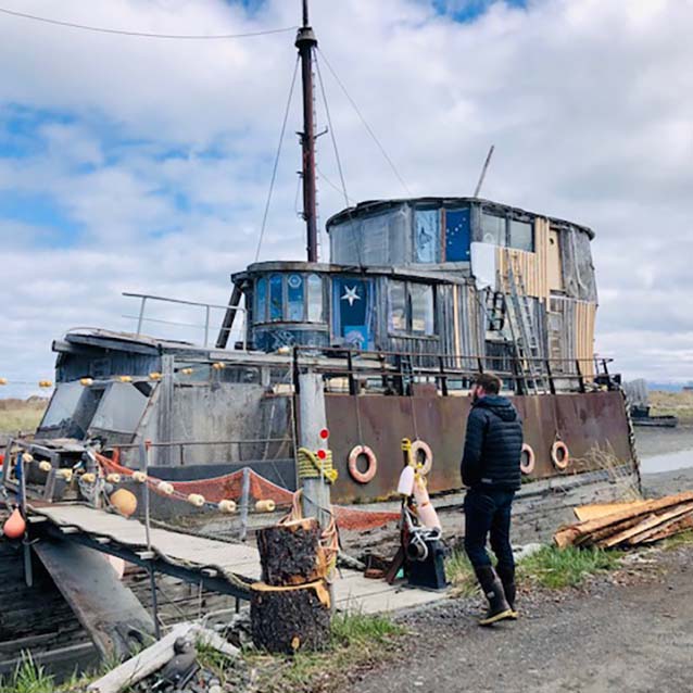 Allen looking at an abandoned boat sitting in water.